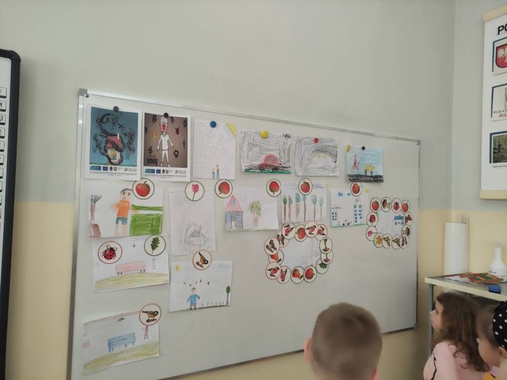 : Rysunki dzieci wykonane podczas warsztatów, przywieszone na tablicy.